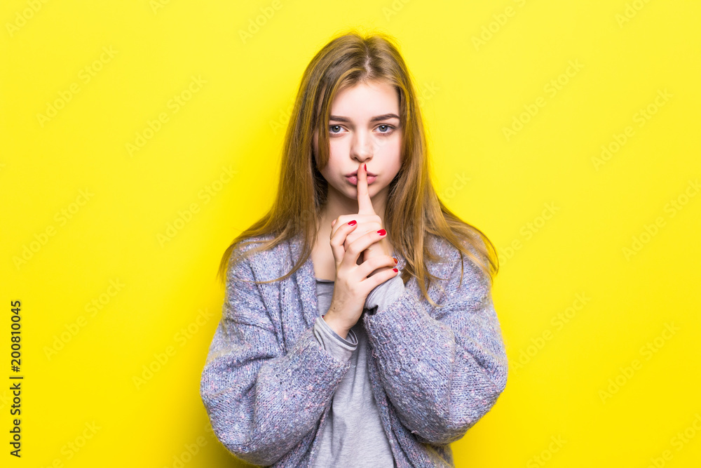 Portrait of teenage girl with silence sign on yellow background Portrait of teenage girl with silence sign on yellow background