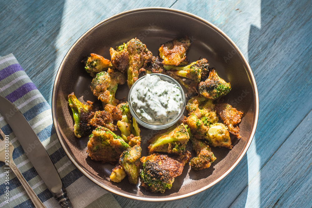 Fried broccoli in batter with spicy white sauce in a plate on a rustic background - top view Fried broccoli in batter with spicy white sauce in a plate on a rustic background - top view