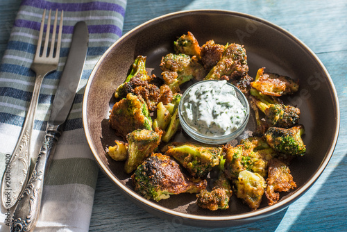 Fried broccoli in batter with spicy white sauce in a plate on a rustic background - top view