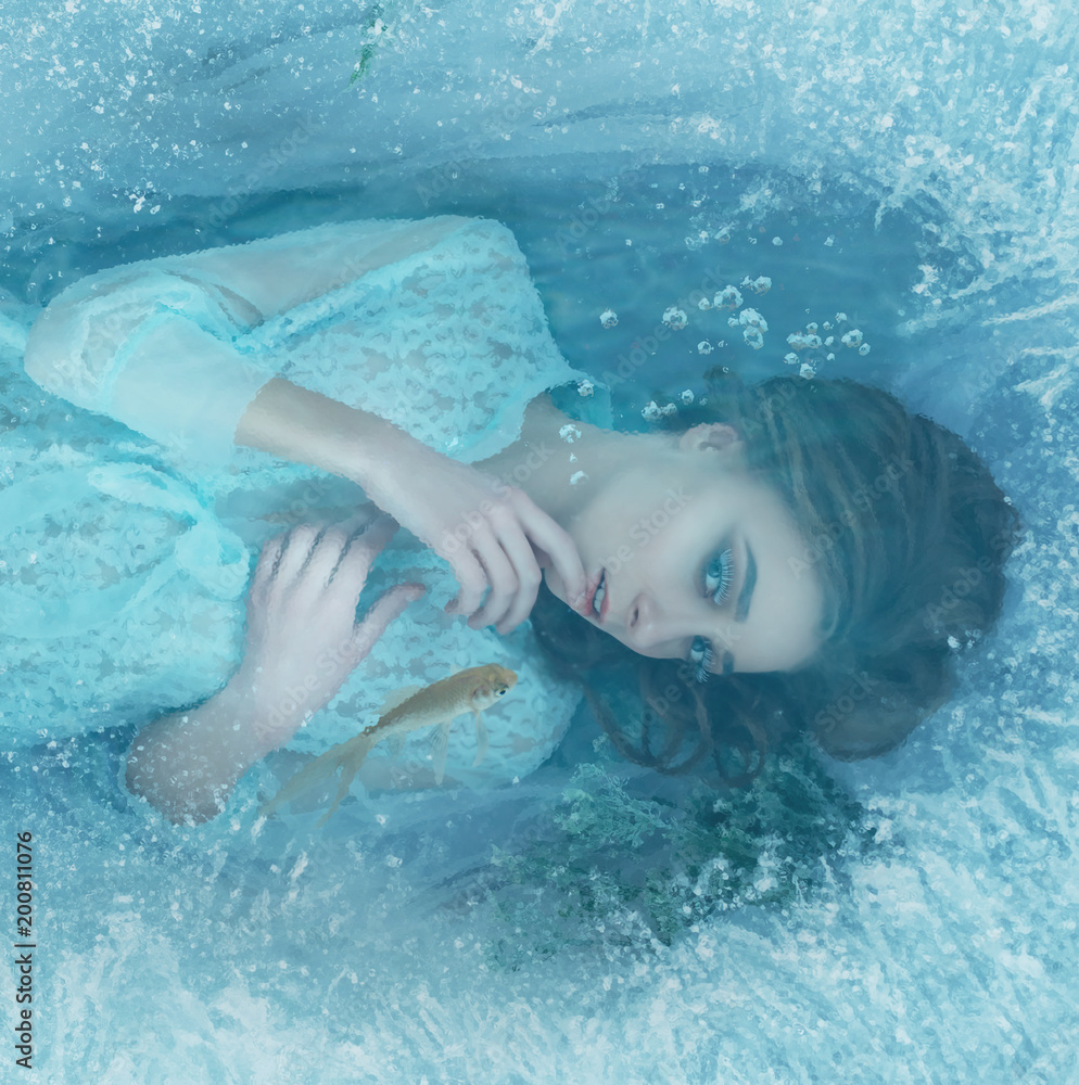 A mermaid girl in a blue vintage dress lies at the bottom of the lake. It is covered with ice edge, fish swim around it. She mysteriously looks through the ice with her finger against her lips