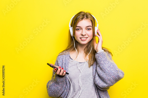 Young beautiful woman enjoying with listening the music in headphones against yellow background photo