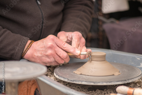 man uses tool to shape clay pot on potters wheel