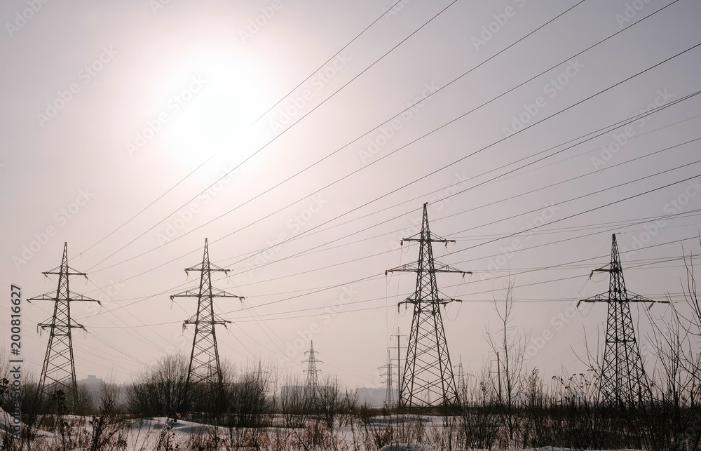 High-voltage towers, transmission line in winter city background.