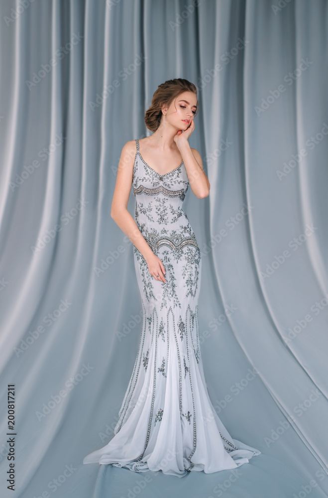 A young girl in a luxurious gray, -silver, sparkling, evening dress posing on the camera. Prom. Stylish bride in rustic style.