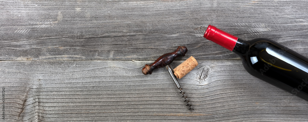 Dark bottle of red wine with vintage corkscrew on rustic wooden planks