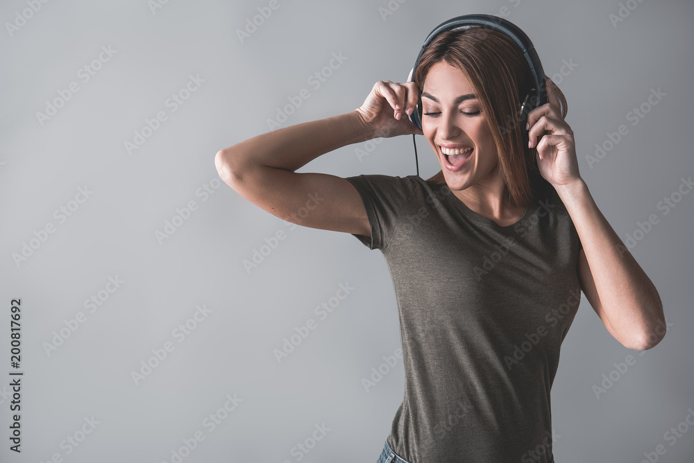Portrait of satisfied woman enjoying melody via earphones. She is moving and looking down. Isolated on background Portrait of satisfied woman enjoying melody via earphones. She is moving and looking down. Isolated on background