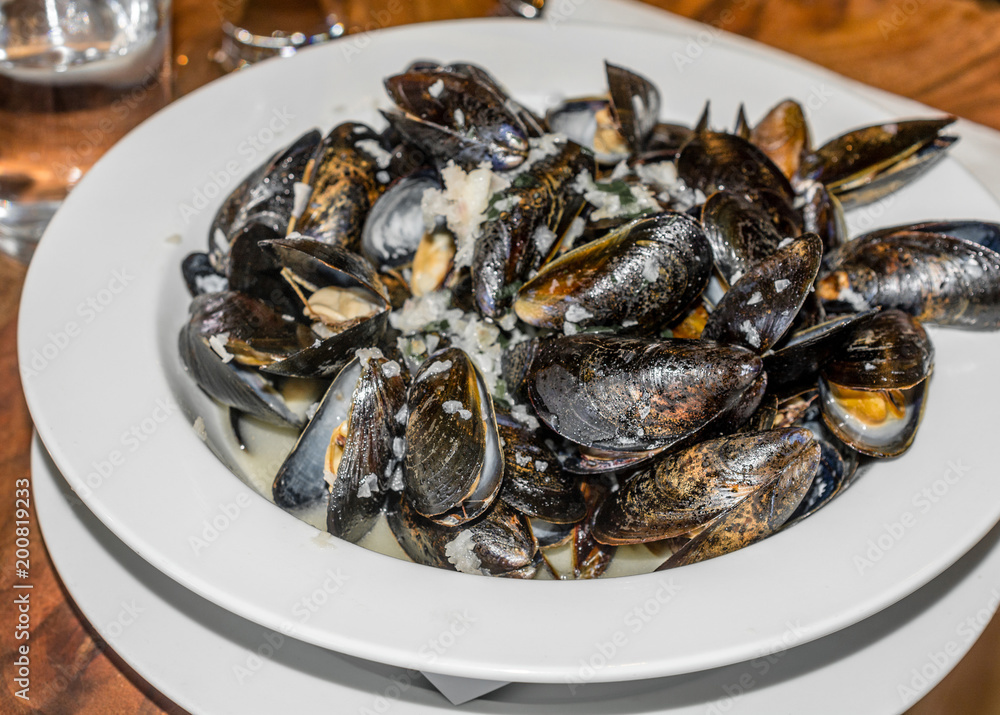 Mussels steamed served in white plate with a glass of water on wooden table Mussels steamed served in white plate with a glass of water on wooden table