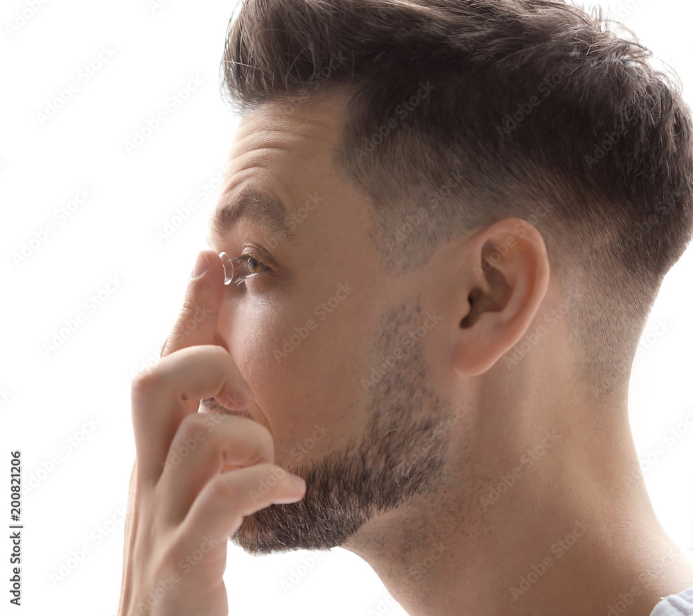 Fototapeta premium Young putting contact lens in his eye on white background