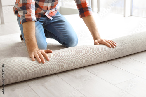 Fotografie Man rolling out new carpet flooring in room