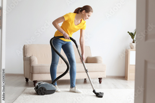 Young woman cleaning carpet with vacuum in living room