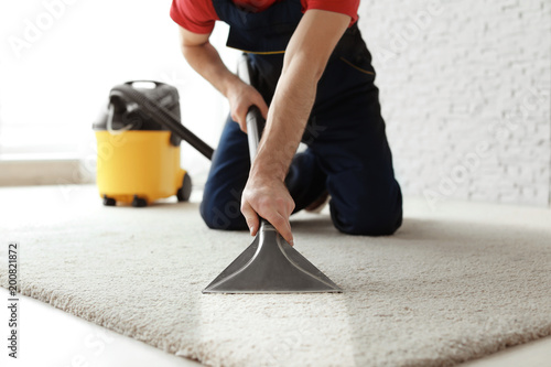 Male worker cleaning carpet with vacuum indoors photo