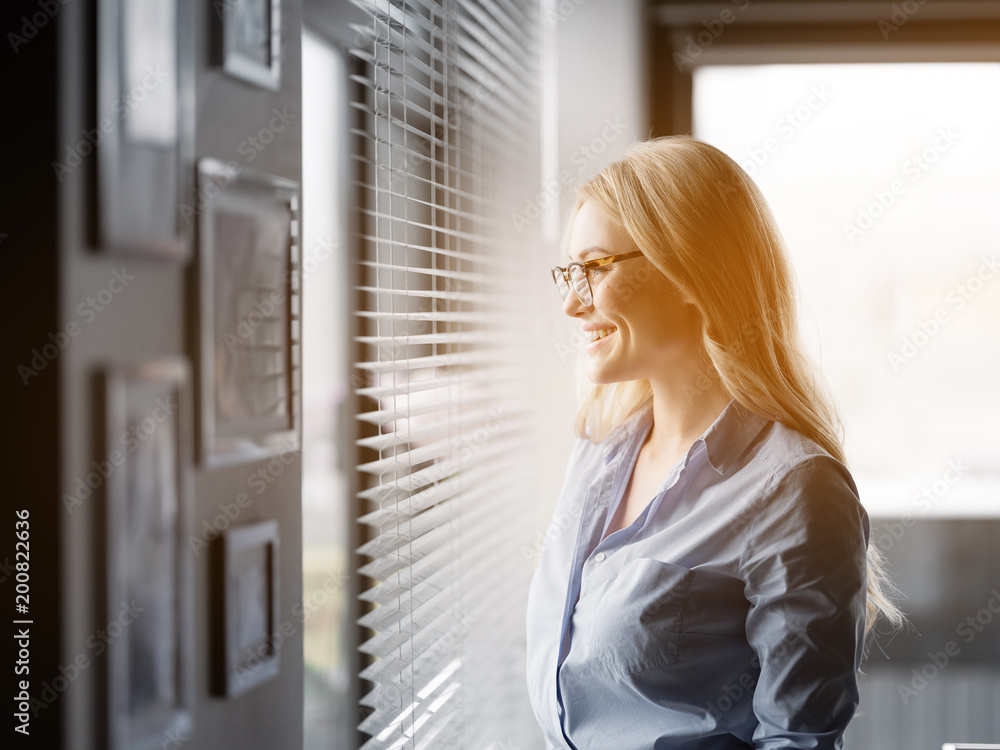 Hope for bright future. Side view profile of happy young woman looking over the window in her office and smiling Hope for bright future. Side view profile of happy young woman looking over the window in her office and smiling