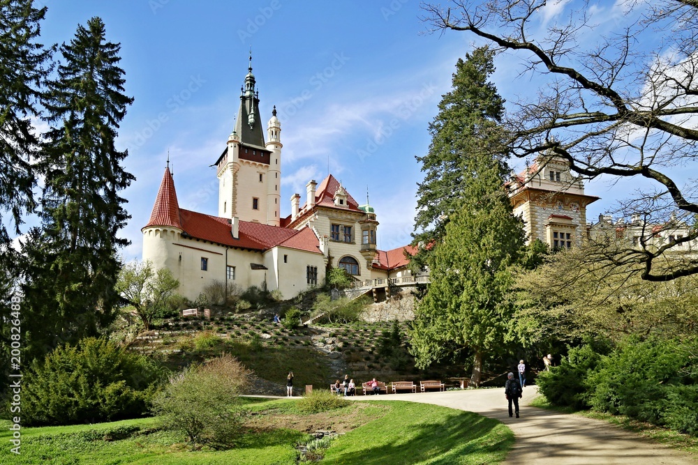 Editorial picture of famous romantic Pruhonice castle, Czech Republic, Europe, standing on hill, garden, sunny spring day, blue sky, green grass, trees, branches, path, people