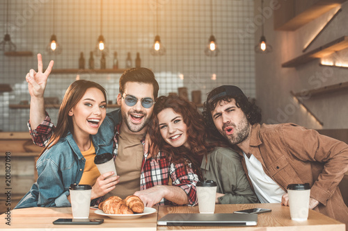 Portrait of excited friends having fun together in coffee shop. They are looking at camera and smiling while embracing