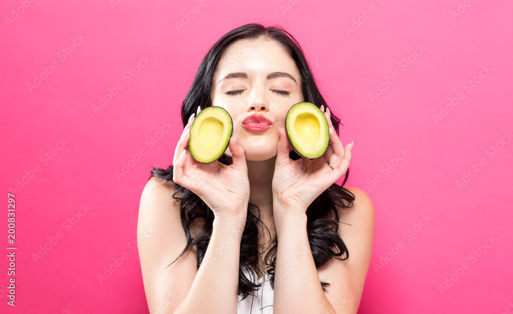 Young woman holding an avocado on a pink background Young woman holding an avocado on a pink background
