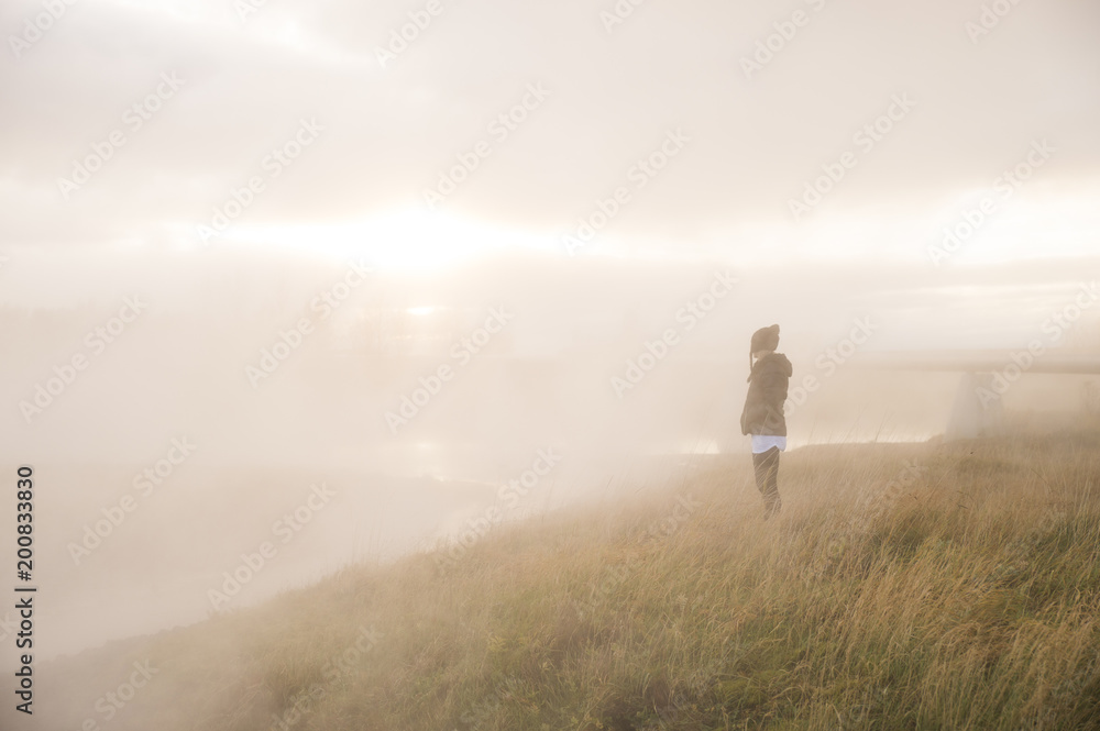 Woman standing in field with natural hot springs steam Woman standing in field with natural hot springs steam