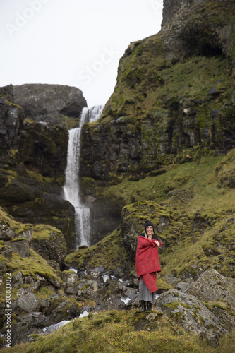 Woman with red blanket standing in front of Icelandic waterfall
