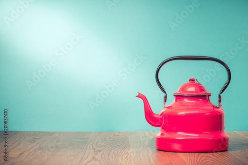 Retro classic red kettle on oak wooden table in front mint green background. Old style filtered photo