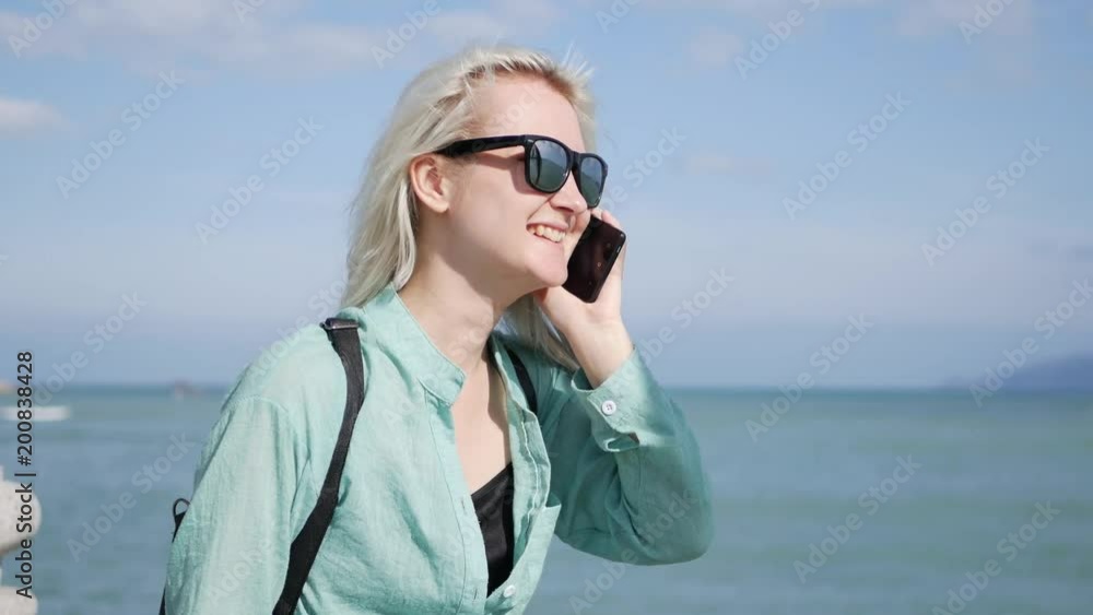 Beautiful slim woman with long blonde hair and green shirt standing and talking on phone over background sea. Beautiful slim woman with long blonde hair and green shirt standing and talking on phone over background sea.
