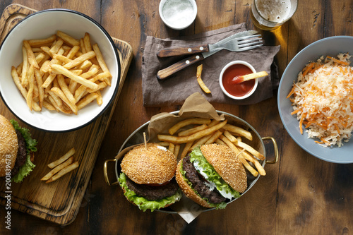 Delicious outdoor table with burger, french fries and salad on wooden table with beer, top view. Outdoors food Concept