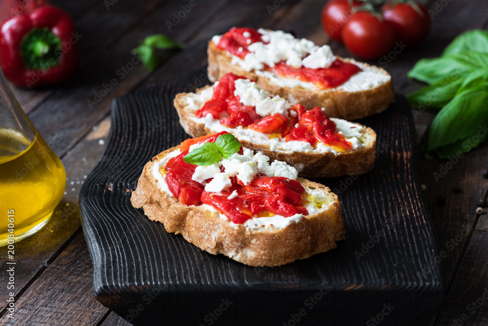 Bruschetta with roasted pepper and goat cheese on black cutting board. Closeup view, selective focus Bruschetta with roasted pepper and goat cheese on black cutting board. Closeup view, selective focus