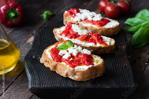 Bruschetta with roasted pepper and goat cheese on black cutting board. Closeup view, selective focus