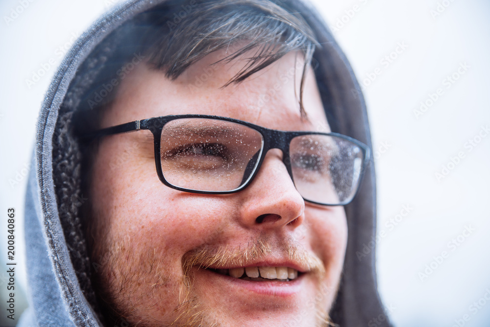 portrait of young adult man with eyeglasses in drops and cover with hood. man with wet hair