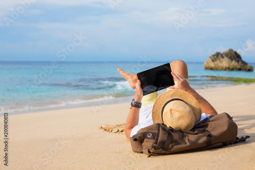 Man lying on the beach and using tablet