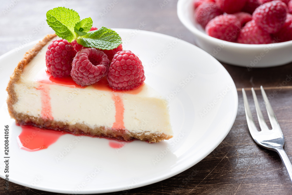 Slice of classical cheesecake with raspberries and berry sauce on white plate. Closeup, selective focus Slice of classical cheesecake with raspberries and berry sauce on white plate. Closeup, selective focus