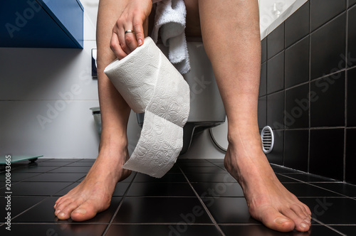 Woman suffers from diarrhea is sitting on toilet bowl photo