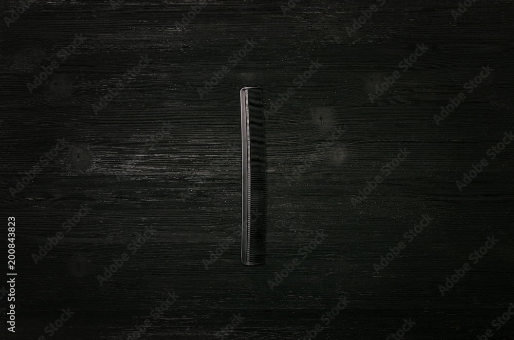Black plastic hair comb isolated on black wooden background.