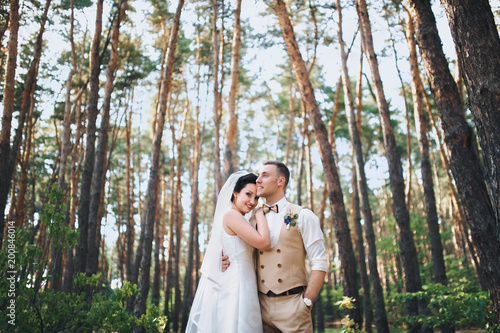 Beautiful newlyweds standing in the woods and hugging each other. Summer wedding. Stylish bride and groom outdoors.