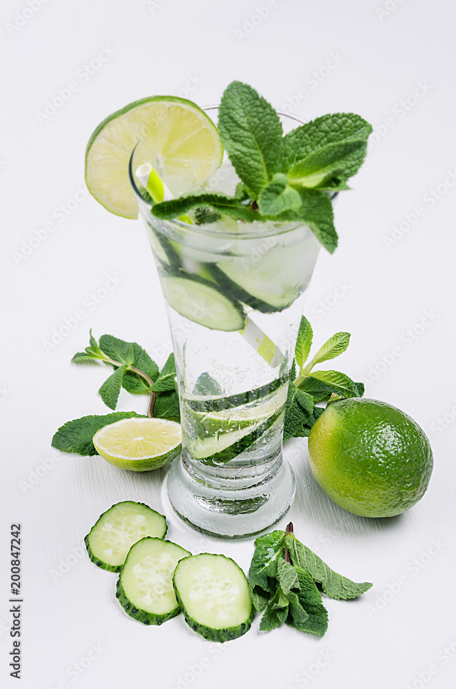 Fototapeta premium Fresh summer organic drink with slices cucumber, ice, lime, mint and ingredients on white wood table, closeup.