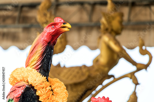 A detail statue of a cock in Buddhist monastery, background golden statue Kinnaris, half-woman from mythology. photo