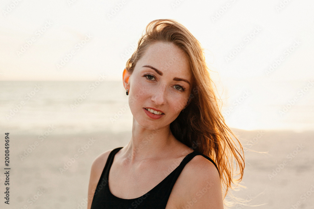 portrait of attractive woman looking at camera on ocean beach during sunset