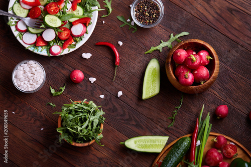 Fresh red radish in wooden bowl among plates with vegetables, herbs and spicies, top view, selective focus.