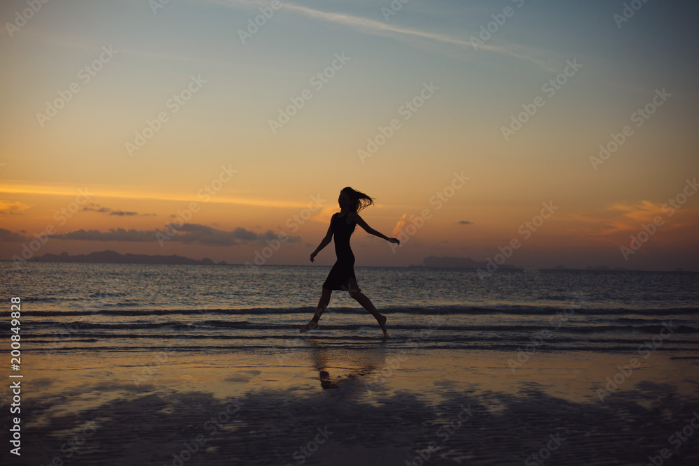 silhouette of woman running on ocean beach during sunset