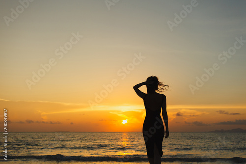 silhouette of woman standing on ocean beach and looking away during sunset