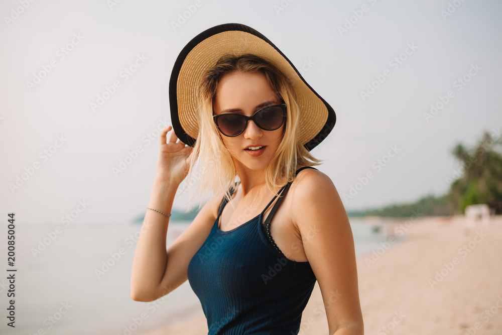 portrait of attractive woman in hat and sunglasses on sandy ocean beach
