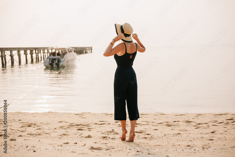 back view of woman standing and touching hat on beach