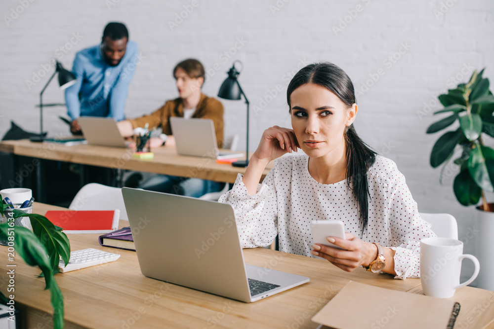 businesswoman with smartphone and colleagues working behind in modern office businesswoman with smartphone and colleagues working behind in modern office