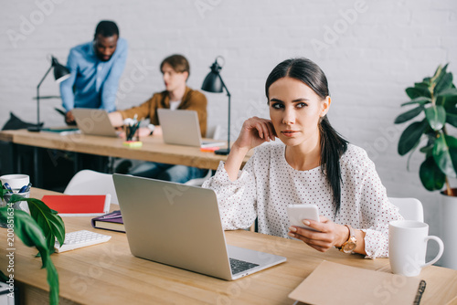 businesswoman with smartphone and colleagues working behind in modern office