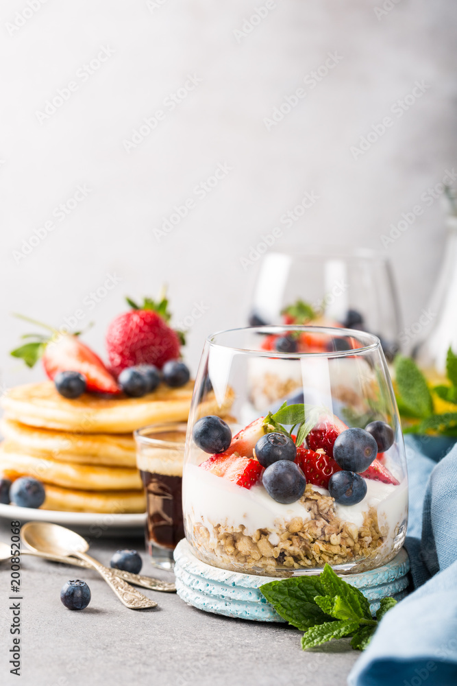 Oatmeal granola with berries and yogurt and panccakes on light gray concrete background. Healthy breakfast food concept with copy space. Oatmeal granola with berries and yogurt and panccakes on light gray concrete background. Healthy breakfast food concept with copy space.