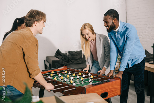 smiling multiethnic business colleagues playing table football in modern office
