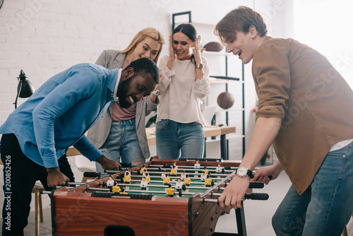 Foto side view of happy multicultural businessmen playing table football in front of