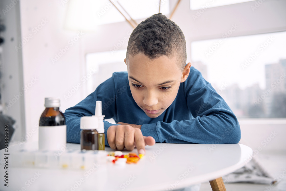 Many pills. Serious afro american boy looking at pills while pointing with finger Many pills. Serious afro american boy looking at pills while pointing with finger