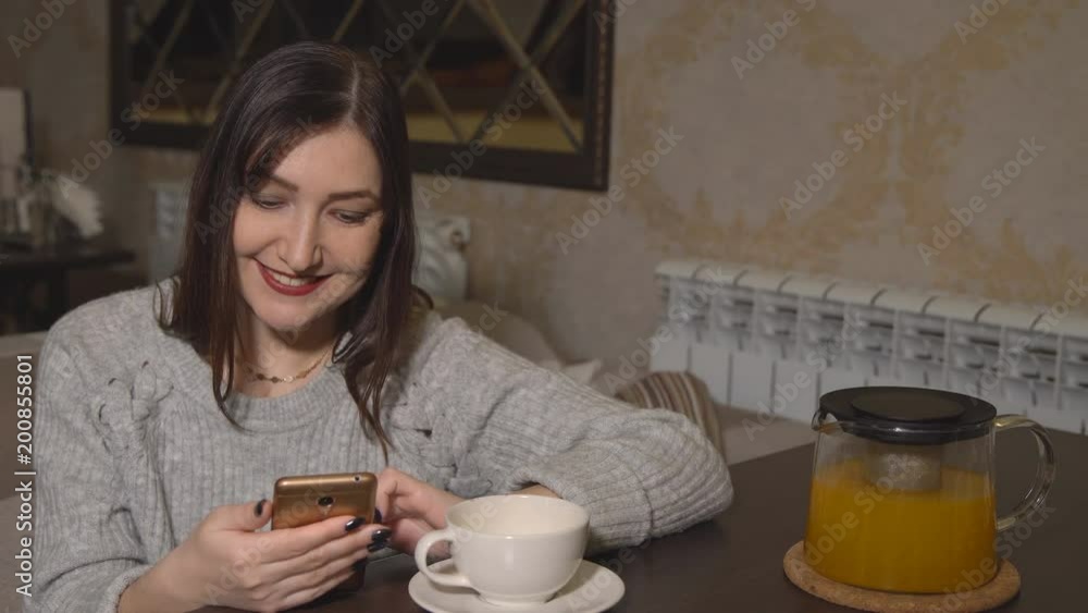 Woman in a cafe at a table drinking tea and leafing through a tape of social networks. Woman in a cafe at a table drinking tea and leafing through a tape of social networks.