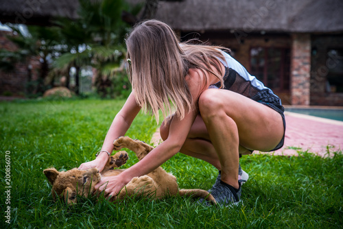 Fototapeta Naklejka Na Ścianę i Meble -  Beautiful young woman play with cute lion on the green grass