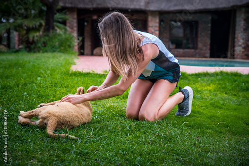 Fototapeta Naklejka Na Ścianę i Meble -  Beautiful young woman play with cute lion on the green grass