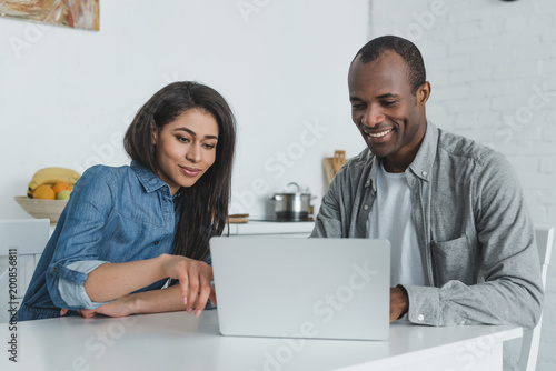 happy african american girlfriend and boyfriend looking at laptop at home